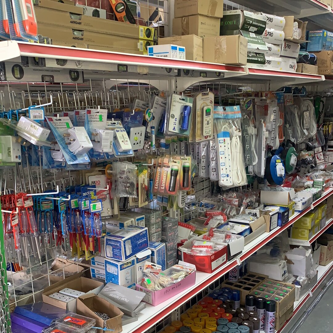 Shop shelving with a pegboard of packaged plug adaptors, trailing extension sockets, a cable reel and screwdriver test pens