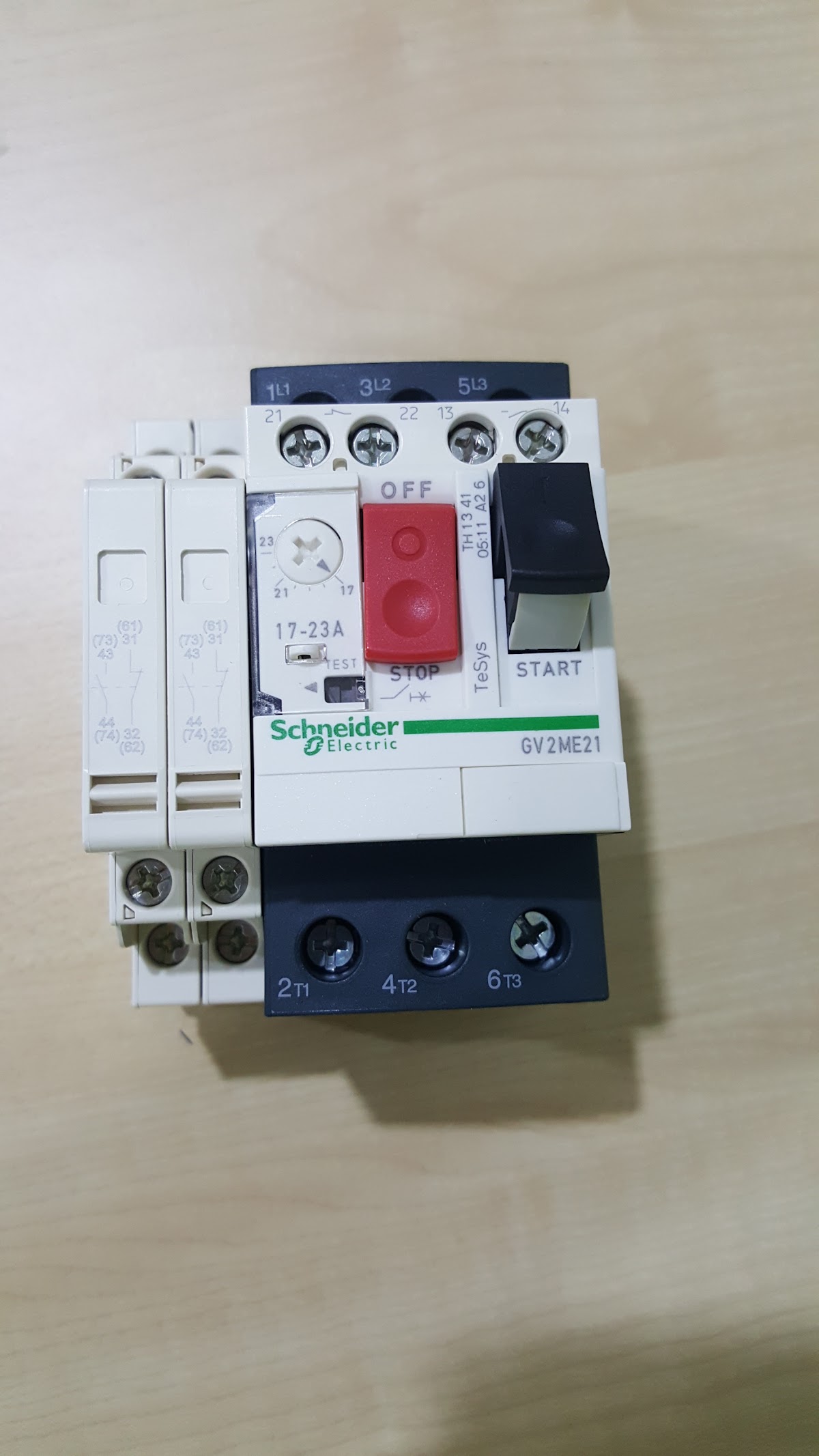 White Schneider GV2ME21 motor circuit breaker with a red stop button on a wooden table