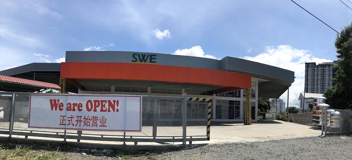 Single-storey building with an orange fascia and SWE lettering behind a fence with a 'We are OPEN' banner