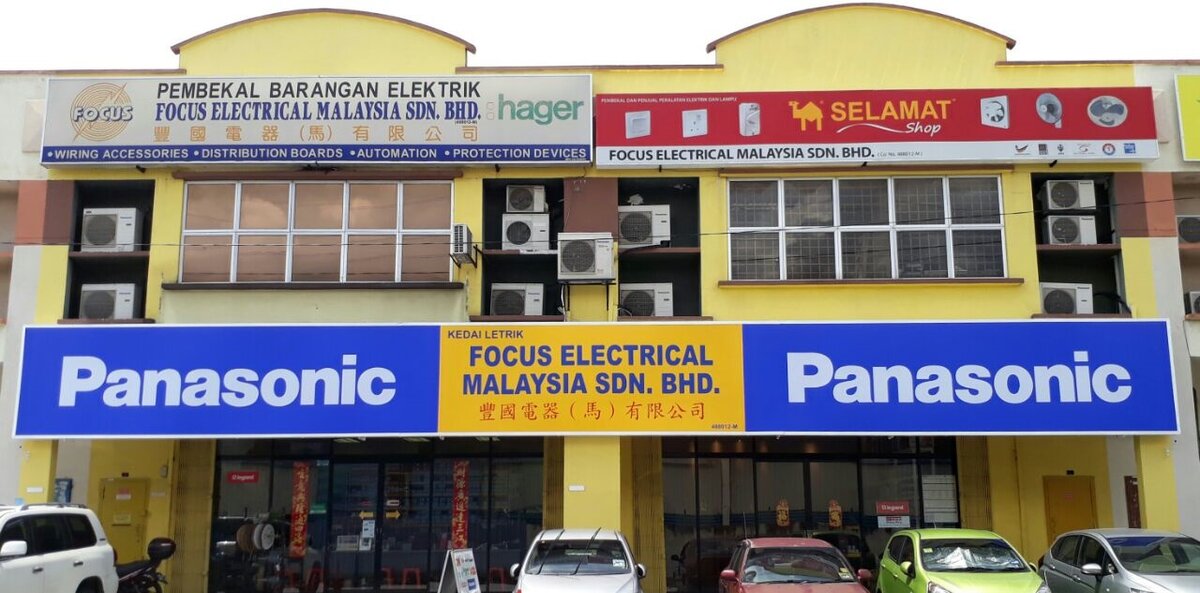 Two-unit yellow shoplot with a Focus Electrical signboard and Hager logo, a red Selamat Shop sign and a long blue Panasonic fascia above glass shopfronts