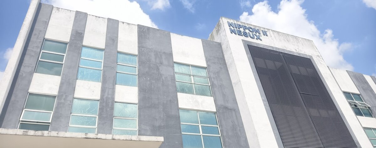 Three-storey grey and white industrial building with NIPPON II NESUX lettering near the top of a tower