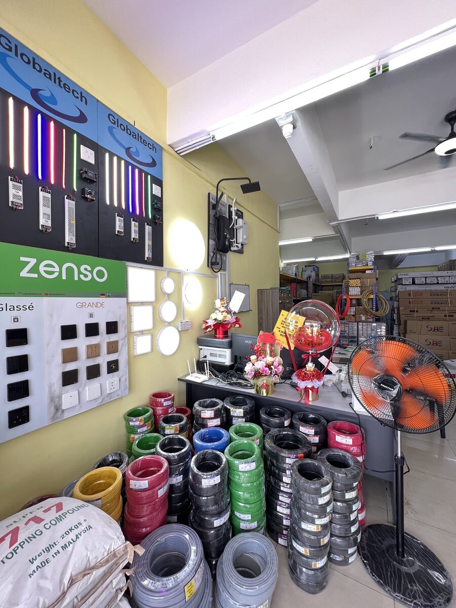 Shop corner with stacks of cable coils in several colours, a board of switches and sockets, LED strip lights and round ceiling lights on the wall
