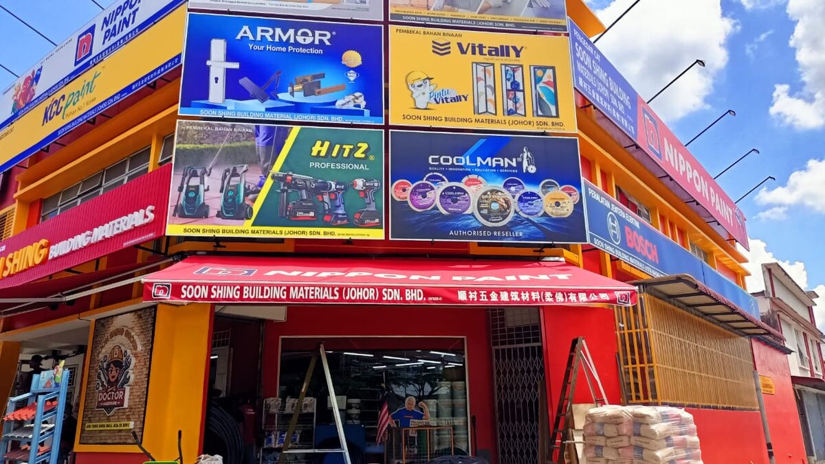 Red and yellow corner shop with Nippon Paint, KCC, Armor, Vitally, Hitz and Coolman signboards and a Soon Shing Building Materials fascia