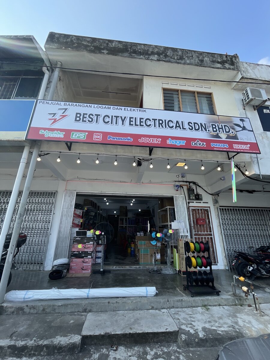 Two-storey shophouse with a Best City Electrical Sdn Bhd signboard carrying brand logos, festoon lights and an open shopfront with fans and wire reels