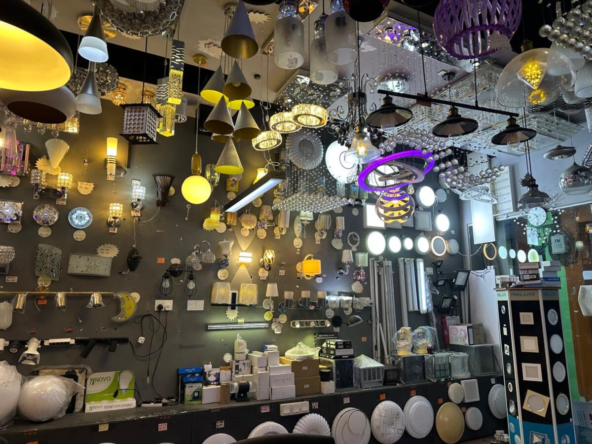Lighting showroom with a dark wall covered in pendant lamps, crystal fittings, wall lights and round ceiling lights, with boxed stock on a counter below