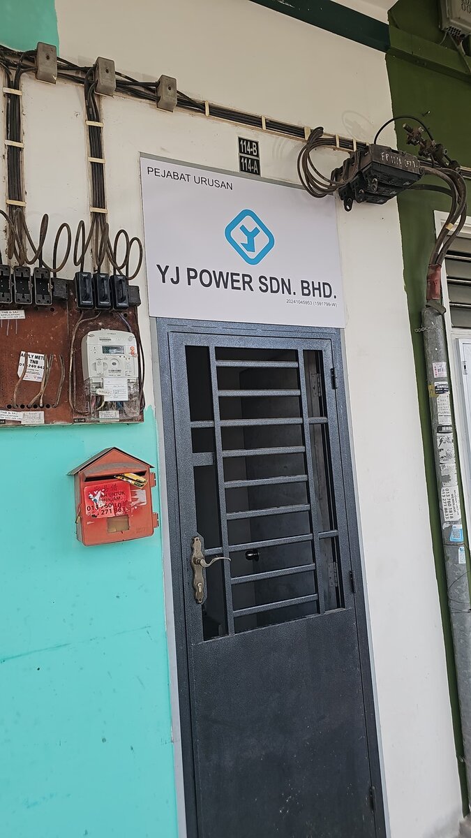 Door marked 114-B with a white sign reading Pejabat Urusan, YJ Power Sdn Bhd, beside wall-mounted electricity meters