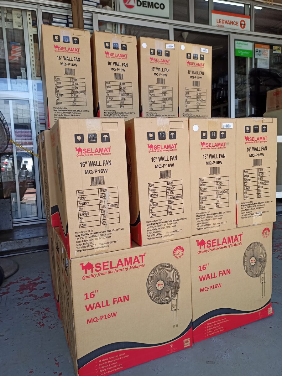 Shop window with Demco and Ledvance Osram signs above a stack of cardboard boxes of 16-inch wall fans