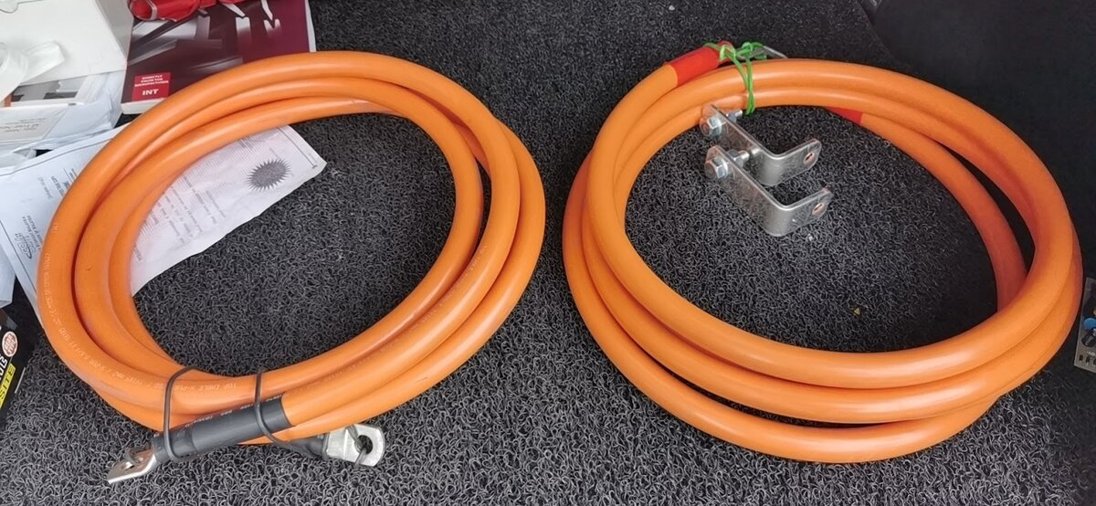 Two coils of thick orange high-current cable, one with crimped lugs visible, and two steel brackets on a dark mat
