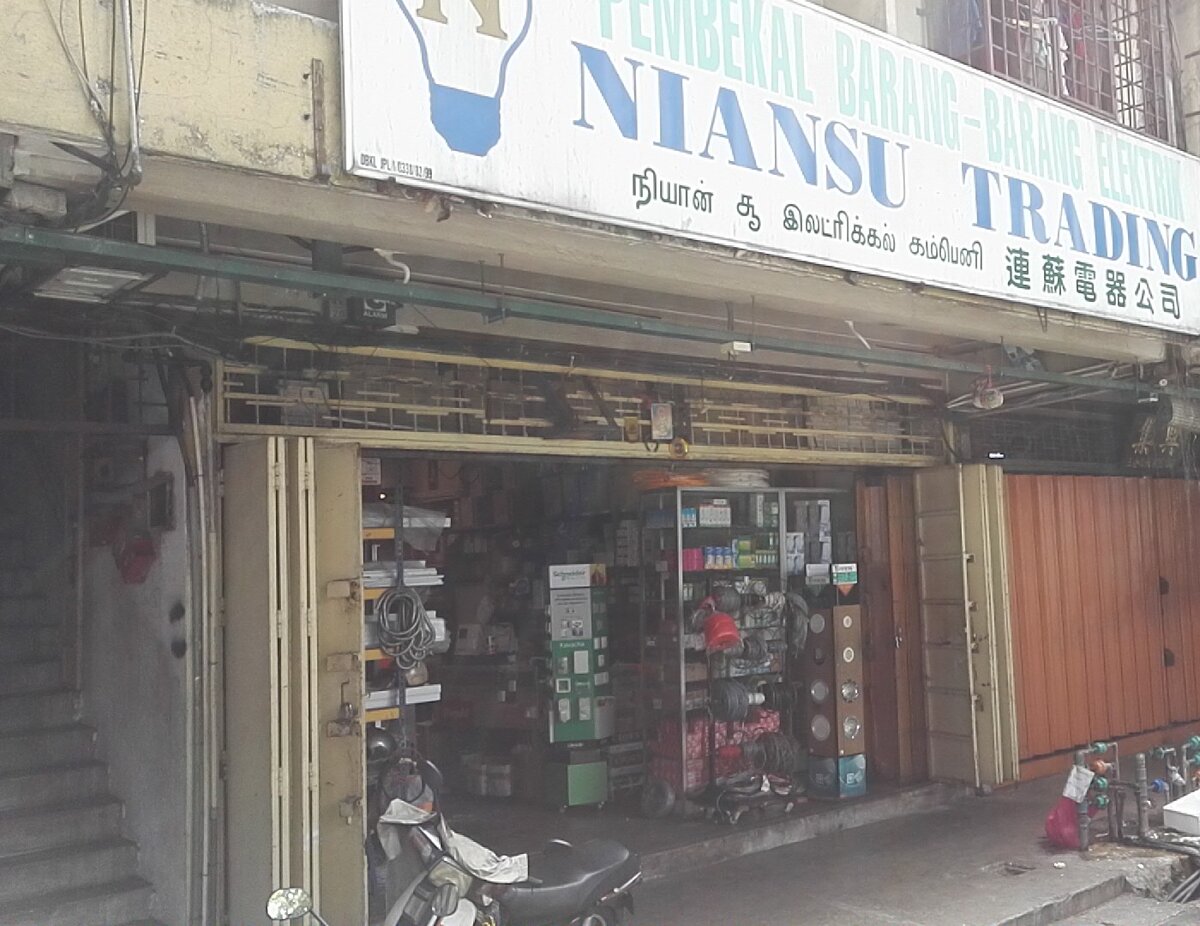 White signboard reading Pembekal Barang-Barang Elektrik Niansu Trading in English, Tamil and Chinese over an electrical shop with a green Schneider display stand