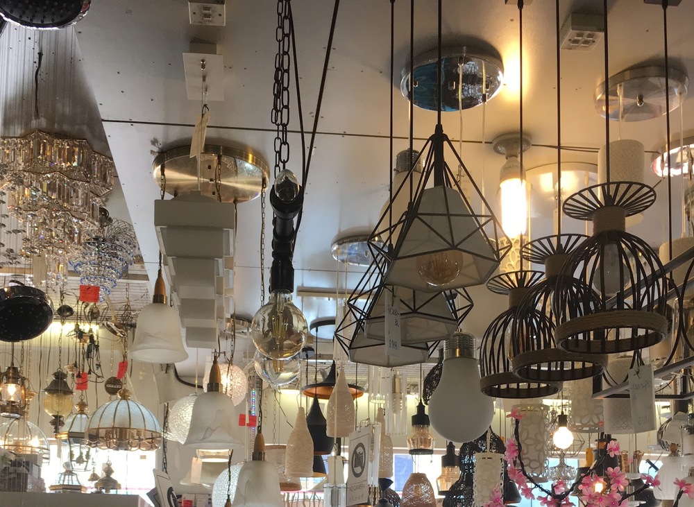 Showroom ceiling crowded with crystal chandeliers, glass pendant lamps and black wire-cage pendant lights