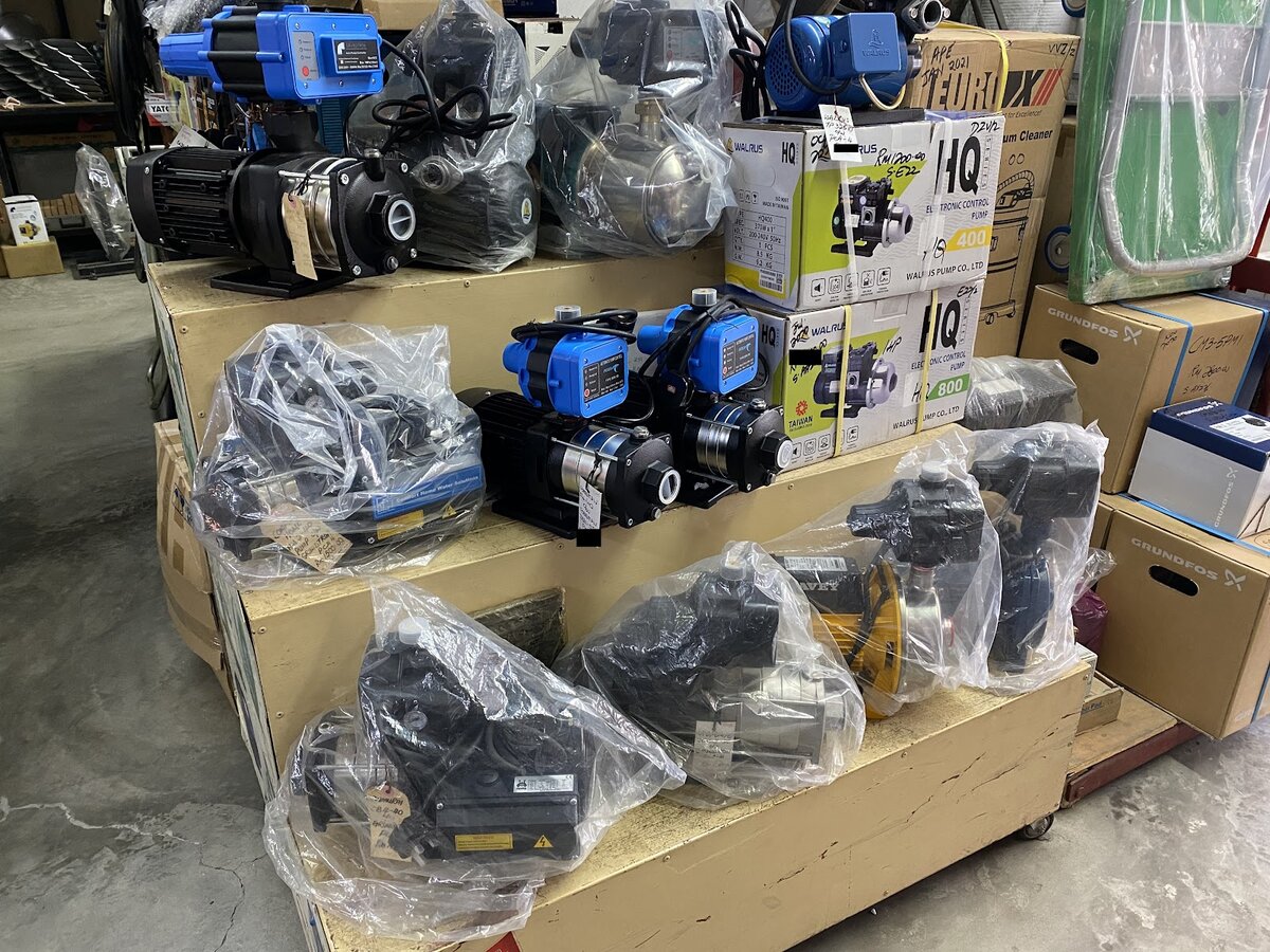 Tiered wooden display of black and blue electric booster pumps, some in plastic bags, with pump cartons stacked to the right