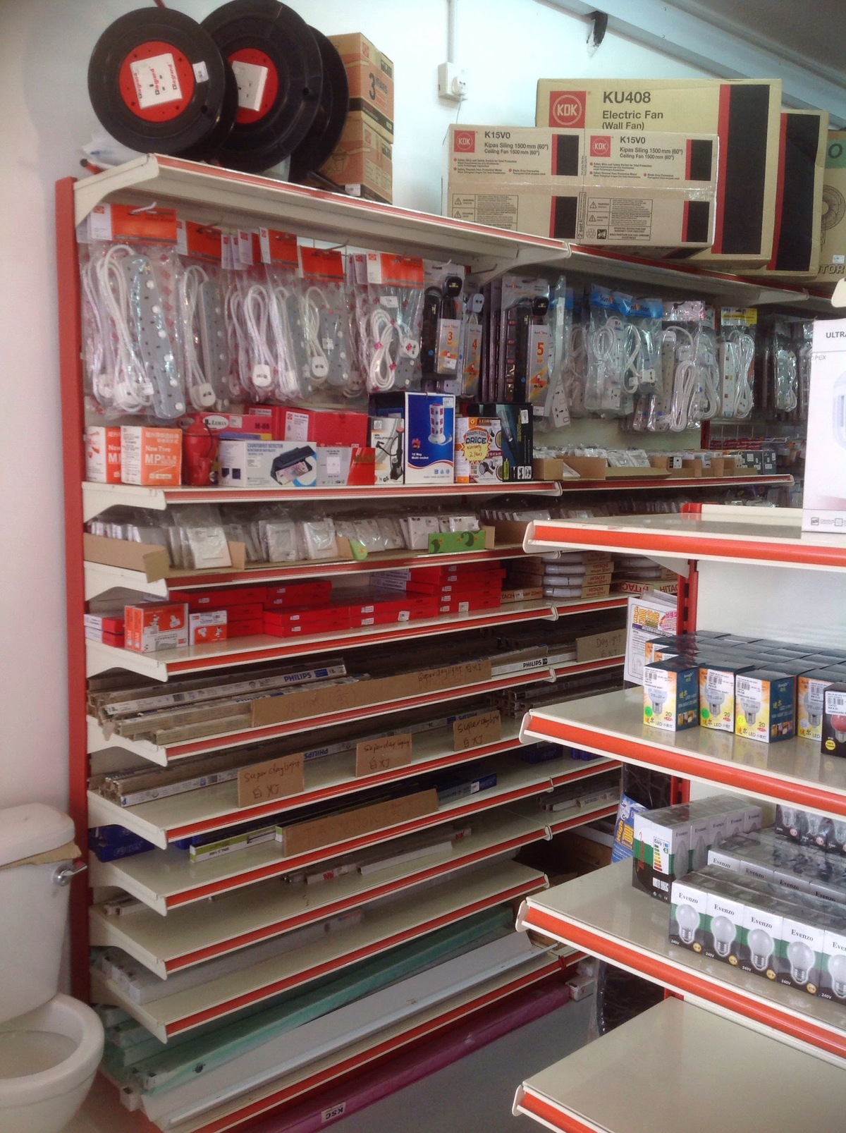 Shop shelving with KDK fan boxes on top, hanging extension-socket packs, boxed lamps and fluorescent tubes on the lower shelves and LED bulb boxes on a side shelf