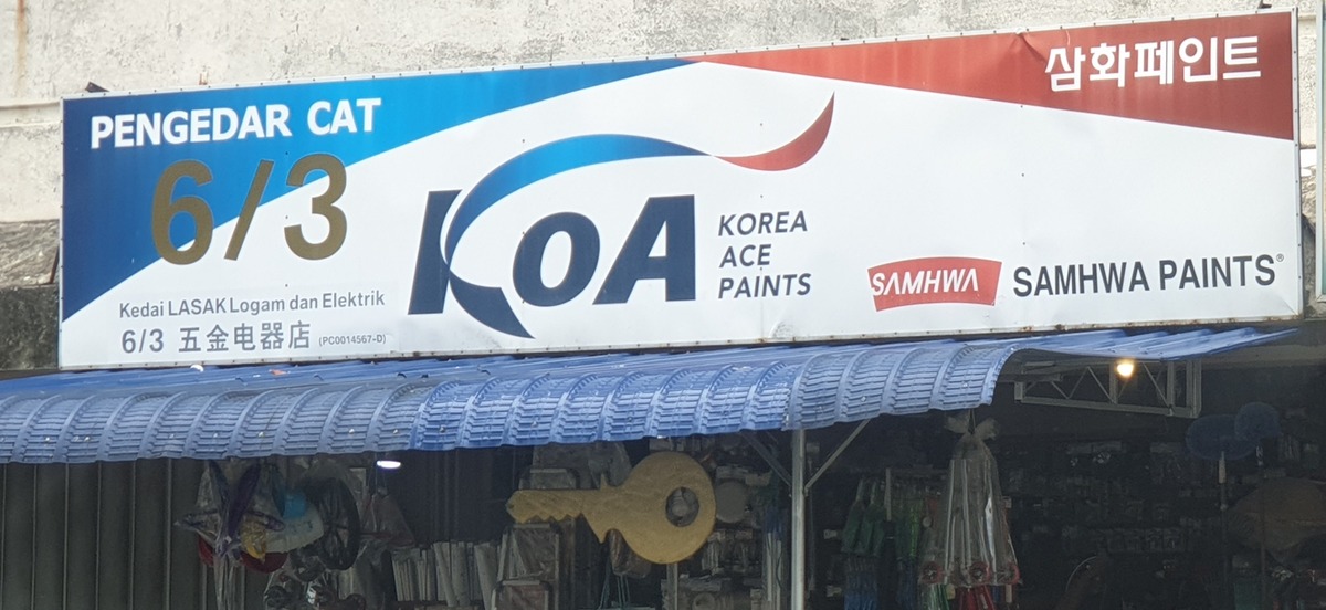 Blue and white shop signboard reading Pengedar Cat 6/3, KOA Korea Ace Paints and Samhwa Paints, with the shop name in Malay and Chinese, above a blue awning and hardware hanging at the shopfront
