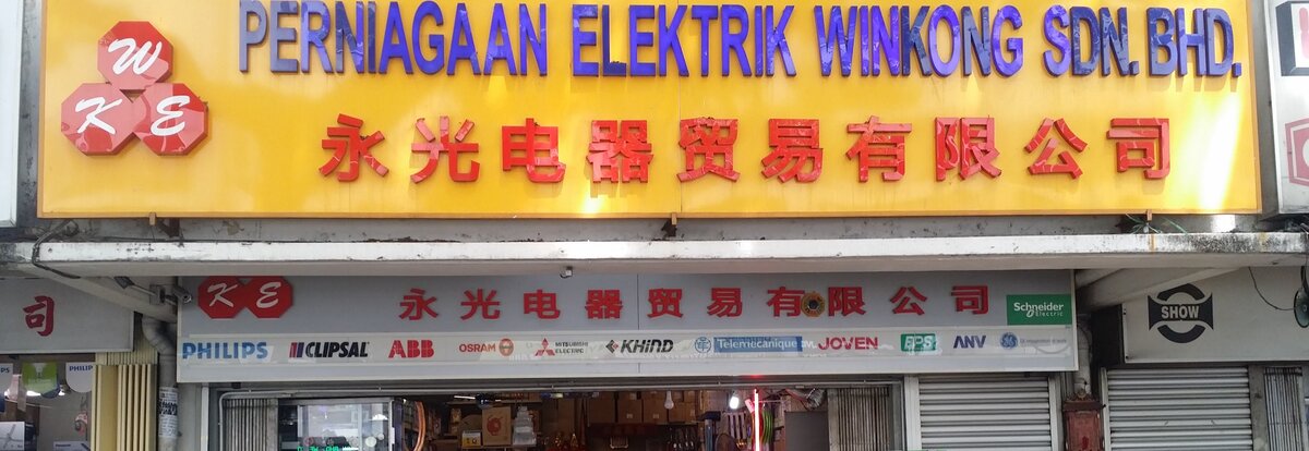 Yellow shop fascia reading Perniagaan Elektrik Winkong Sdn Bhd with red Chinese characters, above a white strip of electrical brand logos and an open shopfront