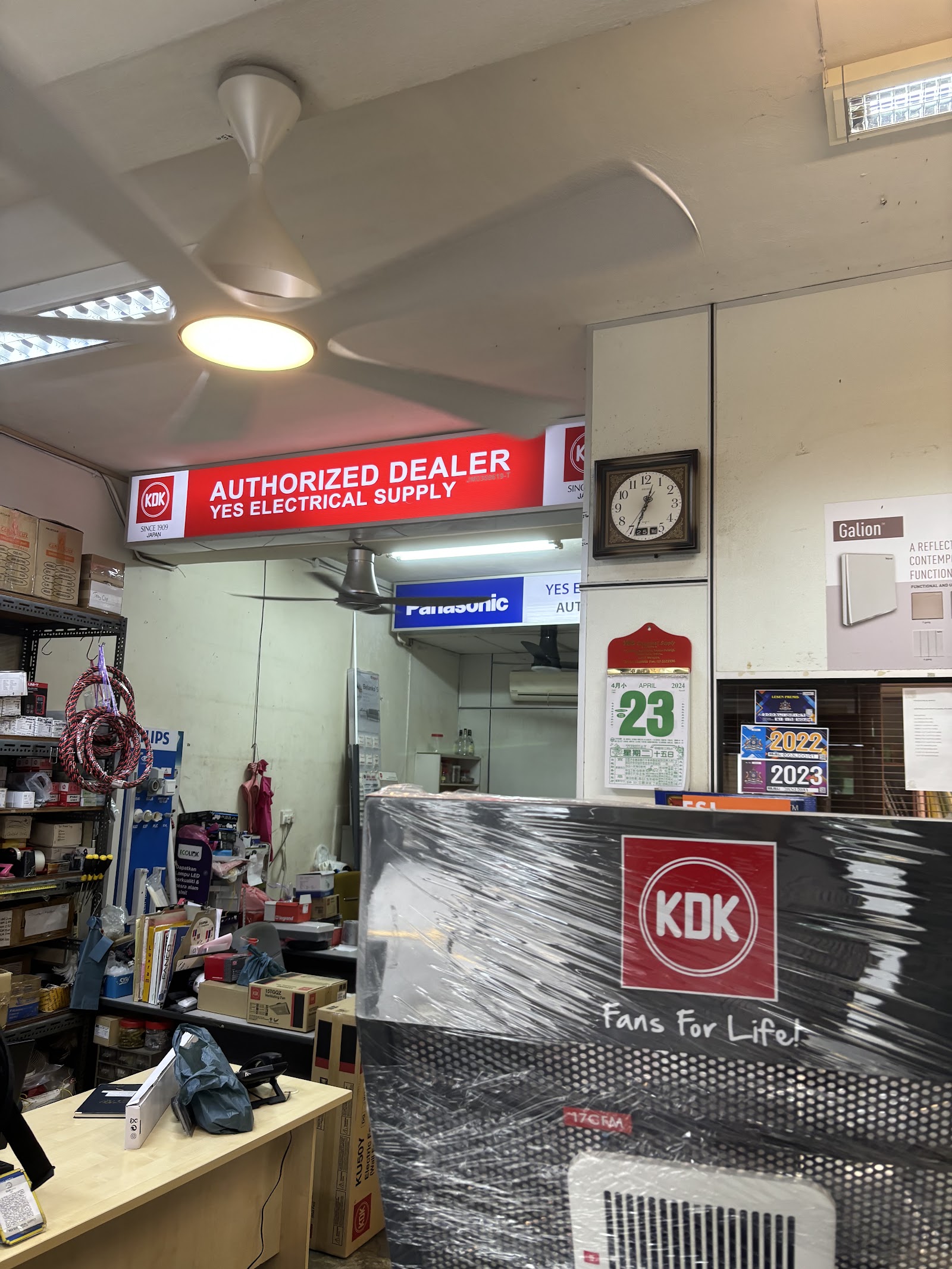 Shop counter under a red KDK Authorized Dealer YES Electrical Supply sign, with a KDK fan box in front