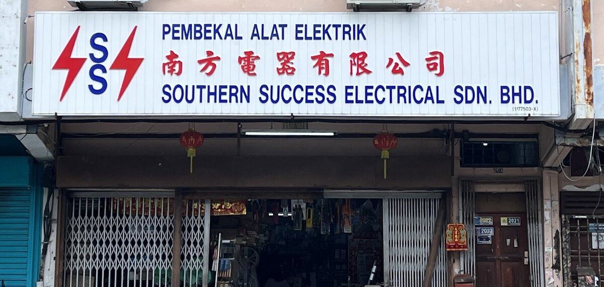 White signboard with a red and blue SS logo reading Pembekal Alat Elektrik, 南方電器有限公司 and Southern Success Electrical Sdn. Bhd. above a shopfront with a folding grille