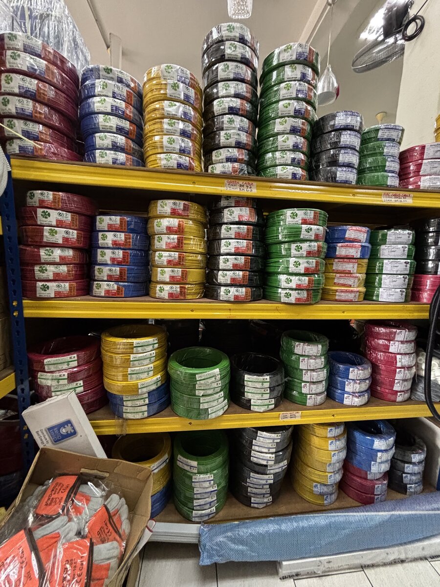 Yellow steel shelving stacked with coils of red, blue, yellow, black and green electrical cable wrapped in plastic with brand labels