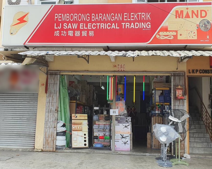 Red signboard reading LJ Saw Electrical Trading above an open shop front with coils of conduit, wire reels, boxed ceiling fans and stand fans