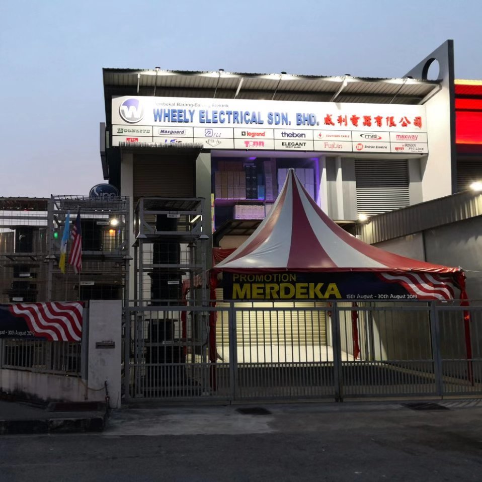 Two-storey shop at dusk with a lit Wheely Electrical signboard and a row of brand logos