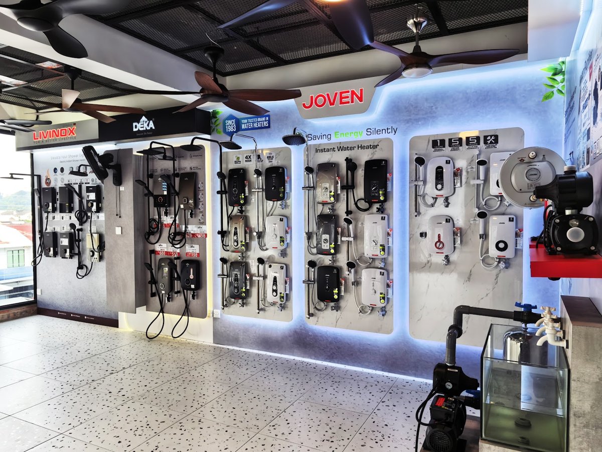 Showroom wall of instant water heaters and shower sets under Joven, Deka and Livinox signs, with ceiling fans overhead and a water pump on a stand