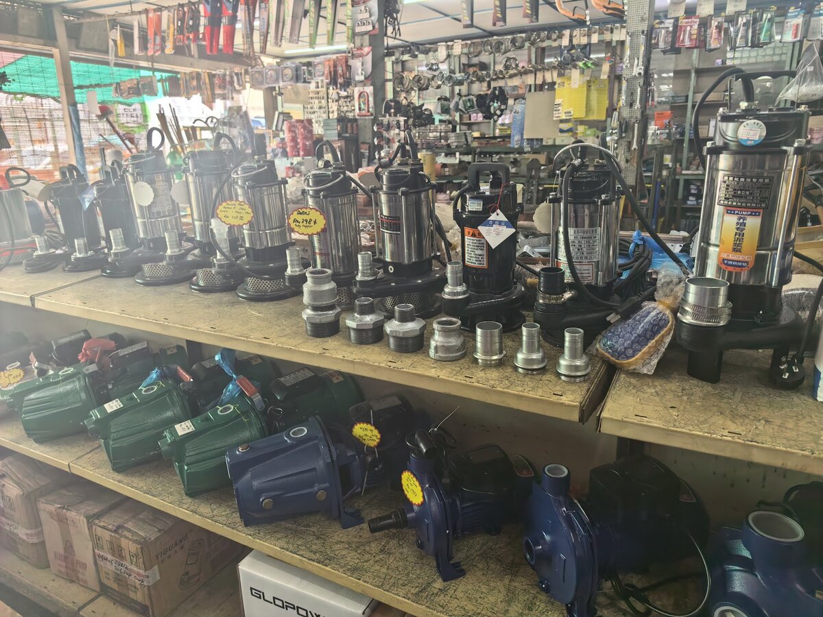 Shelves of stainless-steel submersible pumps above rows of green and blue surface water pumps, with tools hanging behind