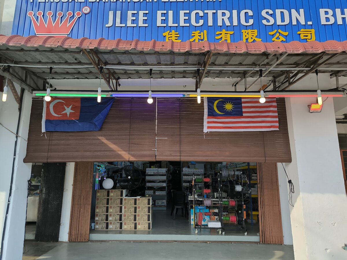Open shopfront under a blue fascia with bamboo blinds, showing racks of coloured wire reels, stacked cartons and a fan inside