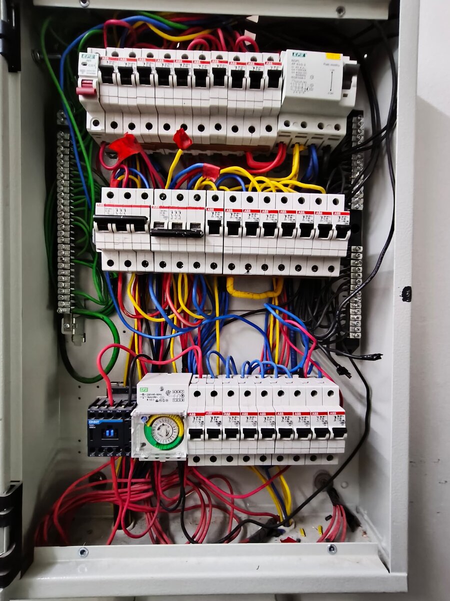 Open grey distribution board with rows of ABB miniature circuit breakers, an EPS C32 breaker with a red toggle and a four-pole RCCB, with red, yellow, blue and green wiring