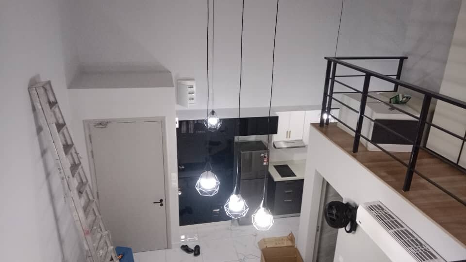 View from an upper floor of a duplex unit down to four wire-cage pendant lights hanging over a kitchen area, with a ladder against the wall