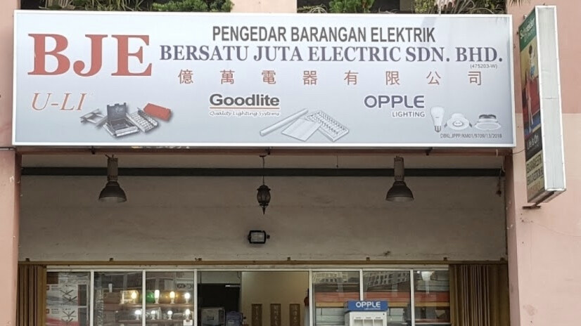 White fascia with red BJE and blue lettering reading Bersatu Juta Electric Sdn Bhd and 億萬電器有限公司 with lighting logos, over an open shopfront with an OPPLE display stand