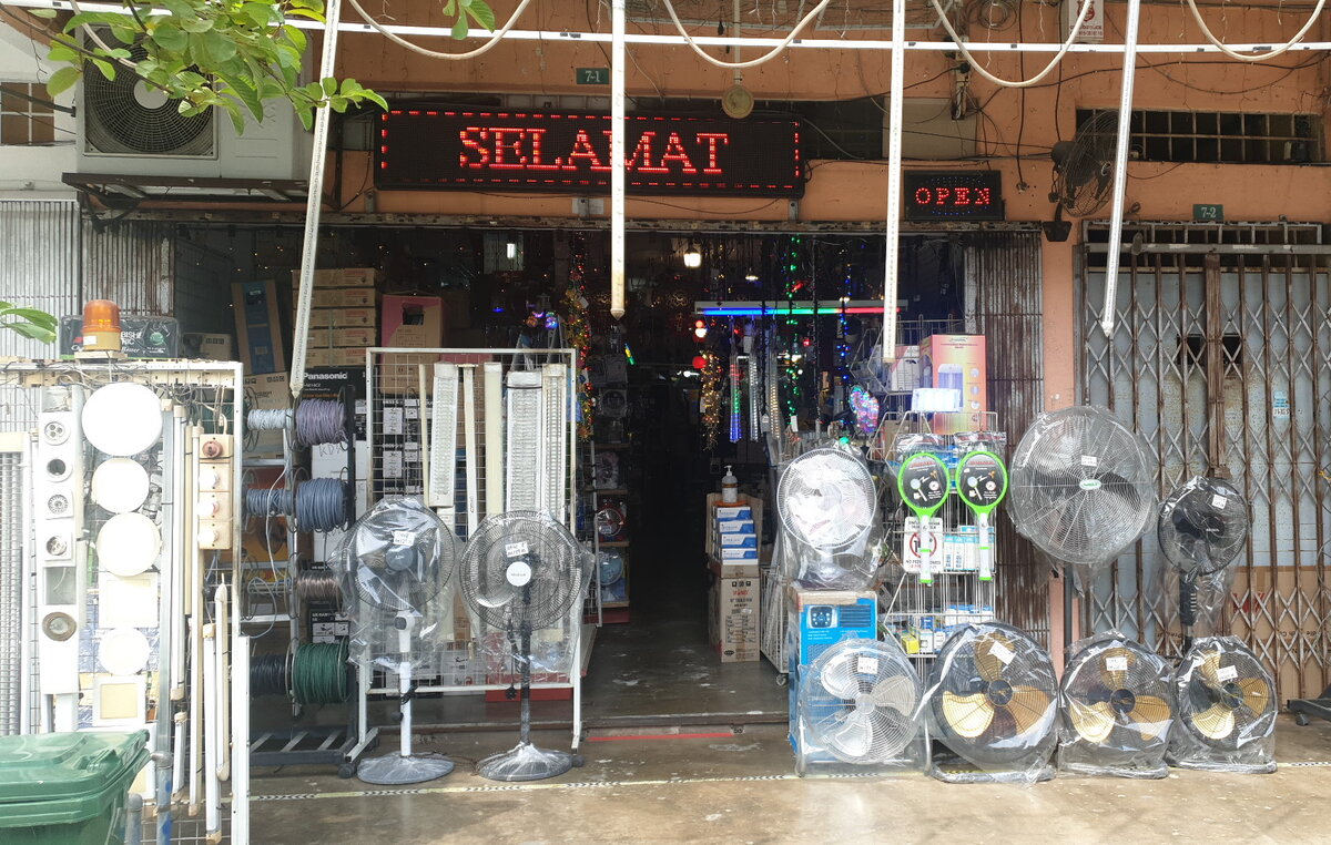 Open shopfront with racks of wire and cable reels, light fittings, stand and wall fans wrapped in plastic and a scrolling LED sign