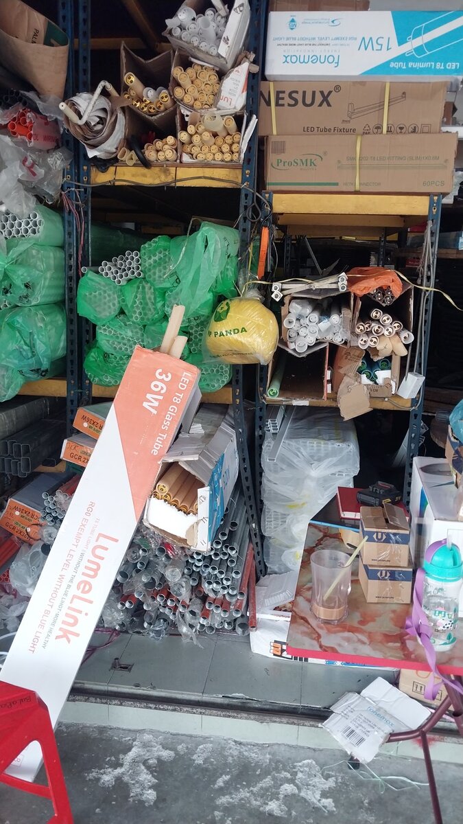 Metal racks holding bundles of PVC and steel conduit, bags of fittings and boxed LED tube lights
