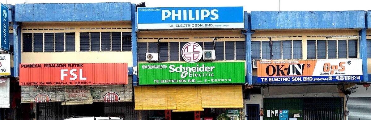 Row of three shop units with red FSL, green Schneider Electric and orange OK-IN OPS fascias and a blue Philips sign above