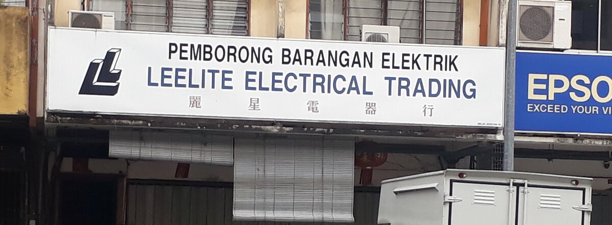 White shop signboard reading Pemborong Barangan Elektrik, Leelite Electrical Trading, with an LL logo and Chinese characters, above lowered blinds
