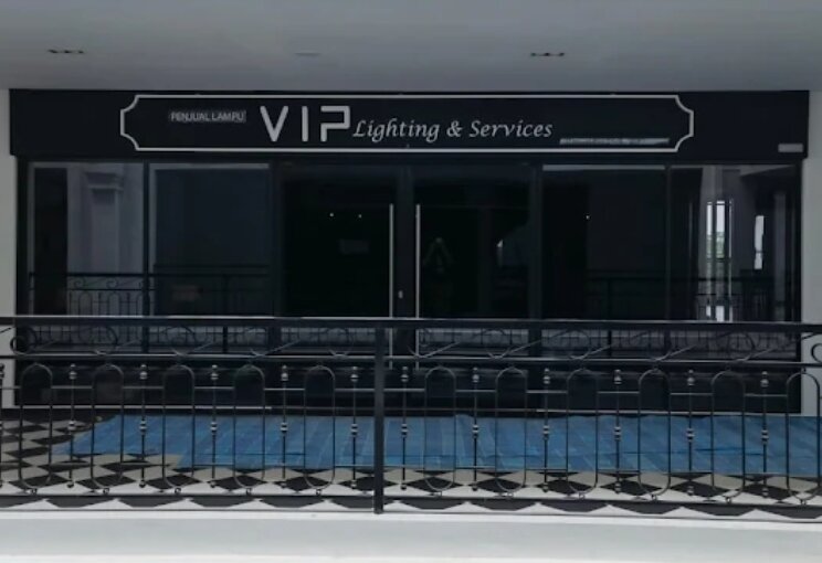 Dark glass shopfront on an upper-floor walkway with a white VIP Lighting & Services sign and a wrought-iron railing