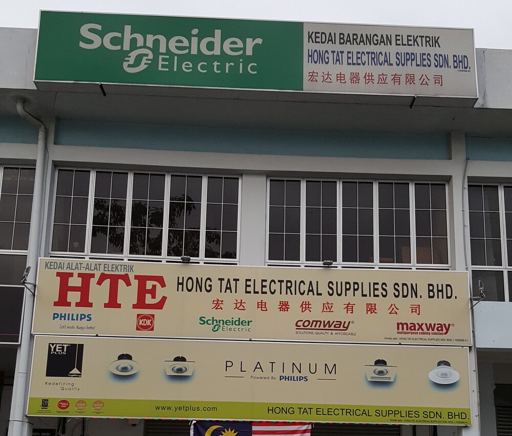 Shopfront with a green Schneider Electric signboard, a cream Hong Tat Electrical Supplies banner with brand logos and a YET Plus downlight banner