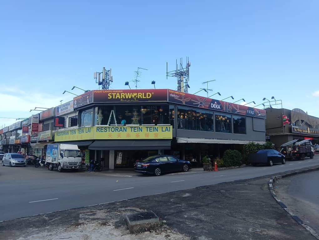 Corner shop block with a red "Pusat Lampu Hiasan Starworld" fascia and a fan banner on the upper floor above a restaurant