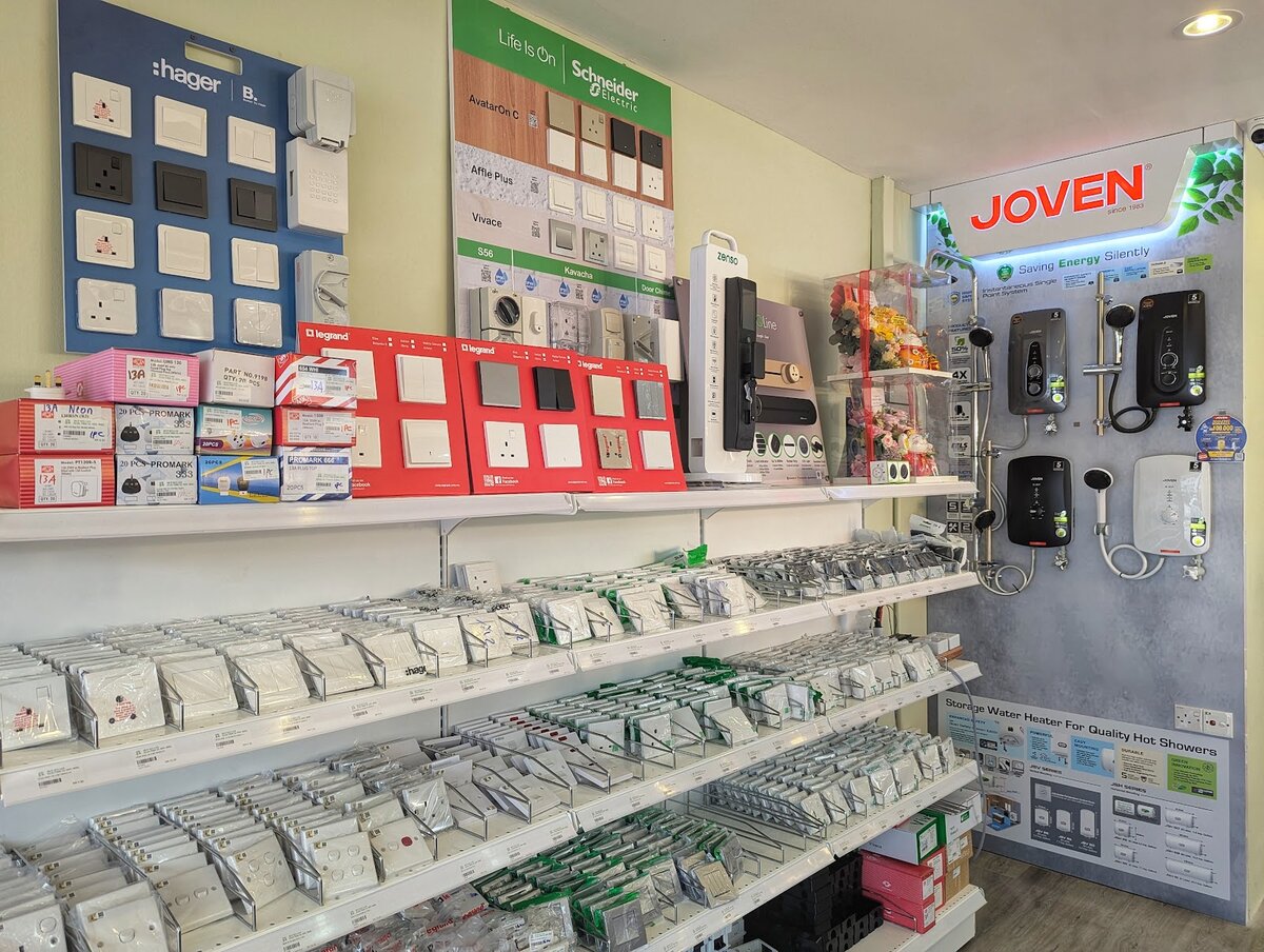 Shop wall with a blue Hager switch board, a green Schneider Electric board of switch ranges, red Legrand display boxes and a Joven water-heater display, above shelves of packed switches