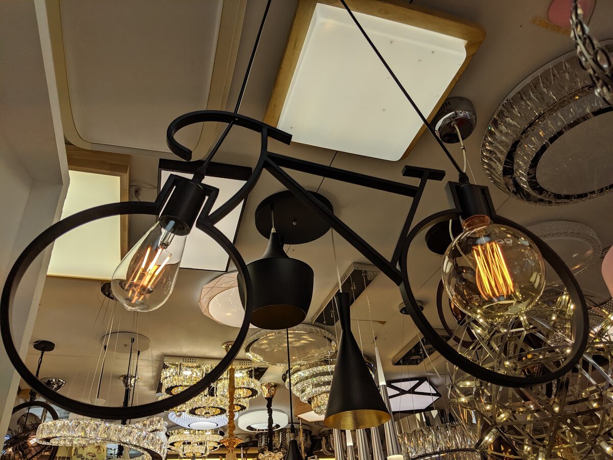 Black bicycle-frame pendant lamp with two filament bulbs hanging among crystal ceiling lights and black pendant shades