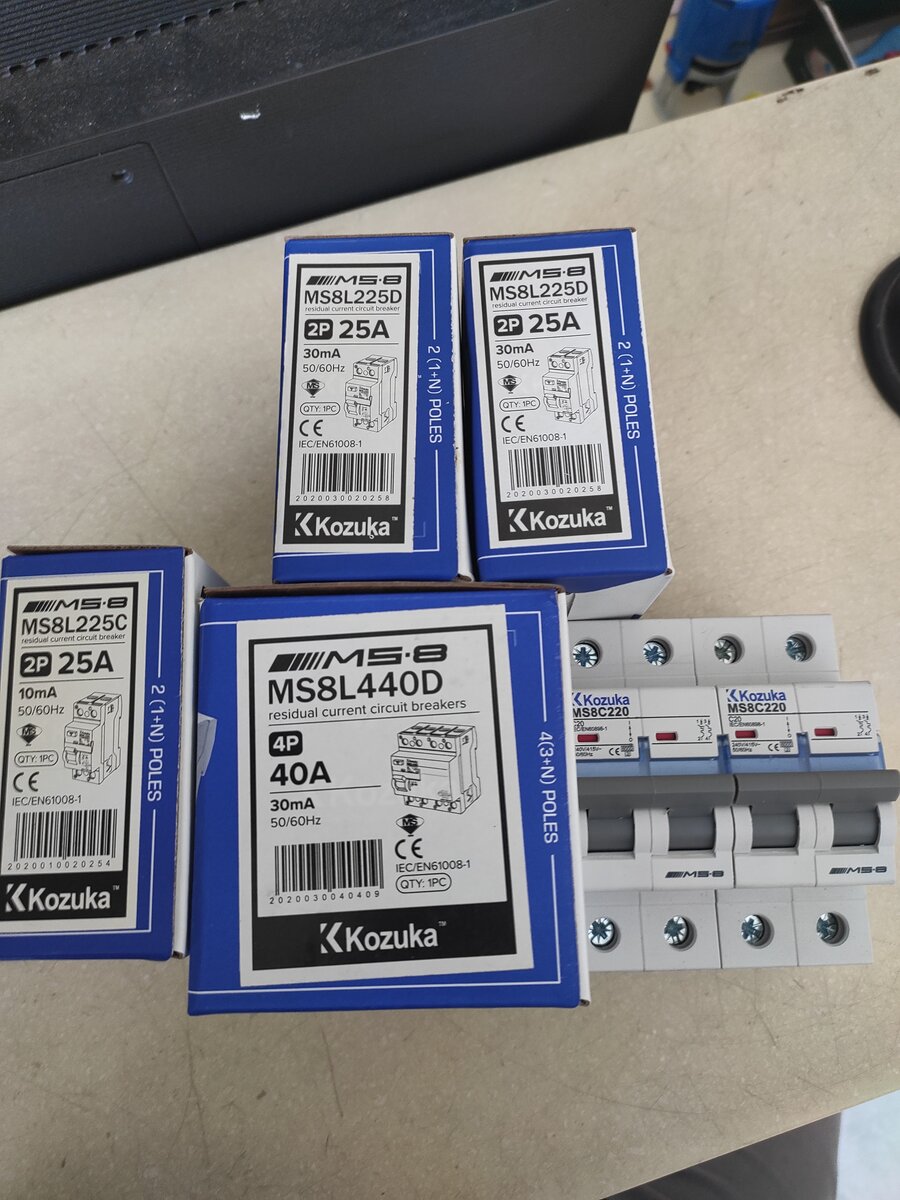 Blue Kozuka boxes labelled MS8L225D, MS8L225C and MS8L440D next to two white miniature circuit breakers on a table