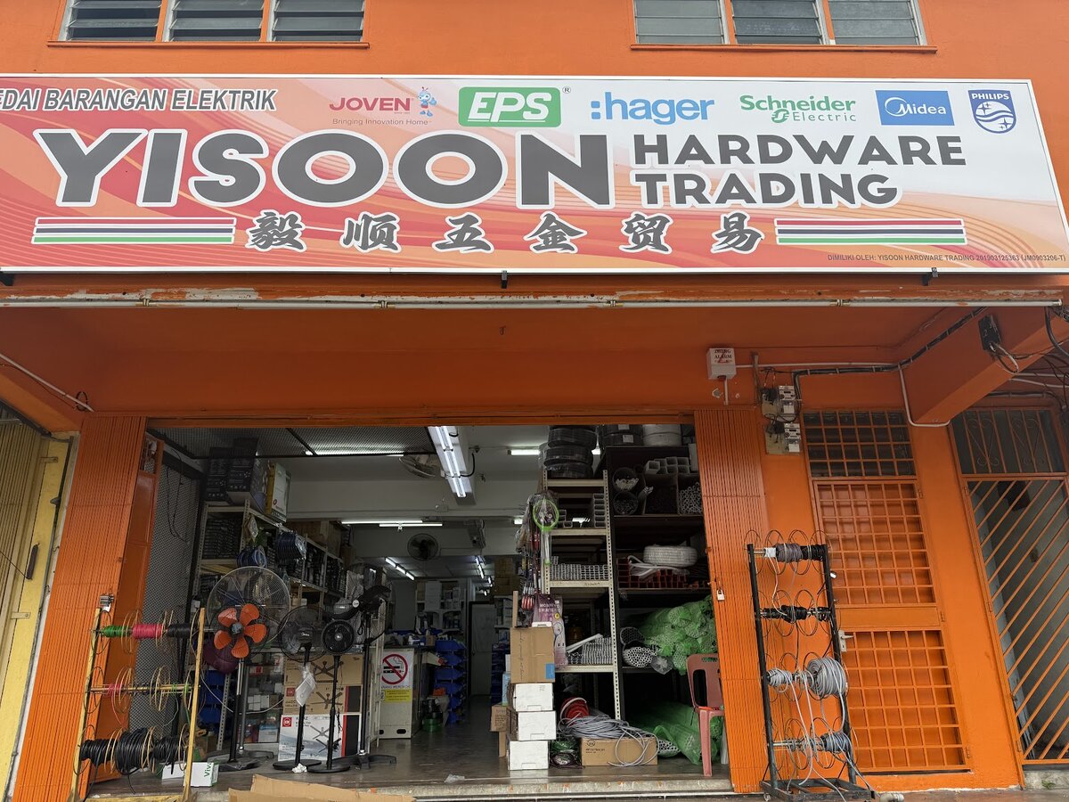 Orange shopfront with a Yisoon Hardware Trading signboard carrying electrical brand logos, standing fans and reels of cable at the entrance