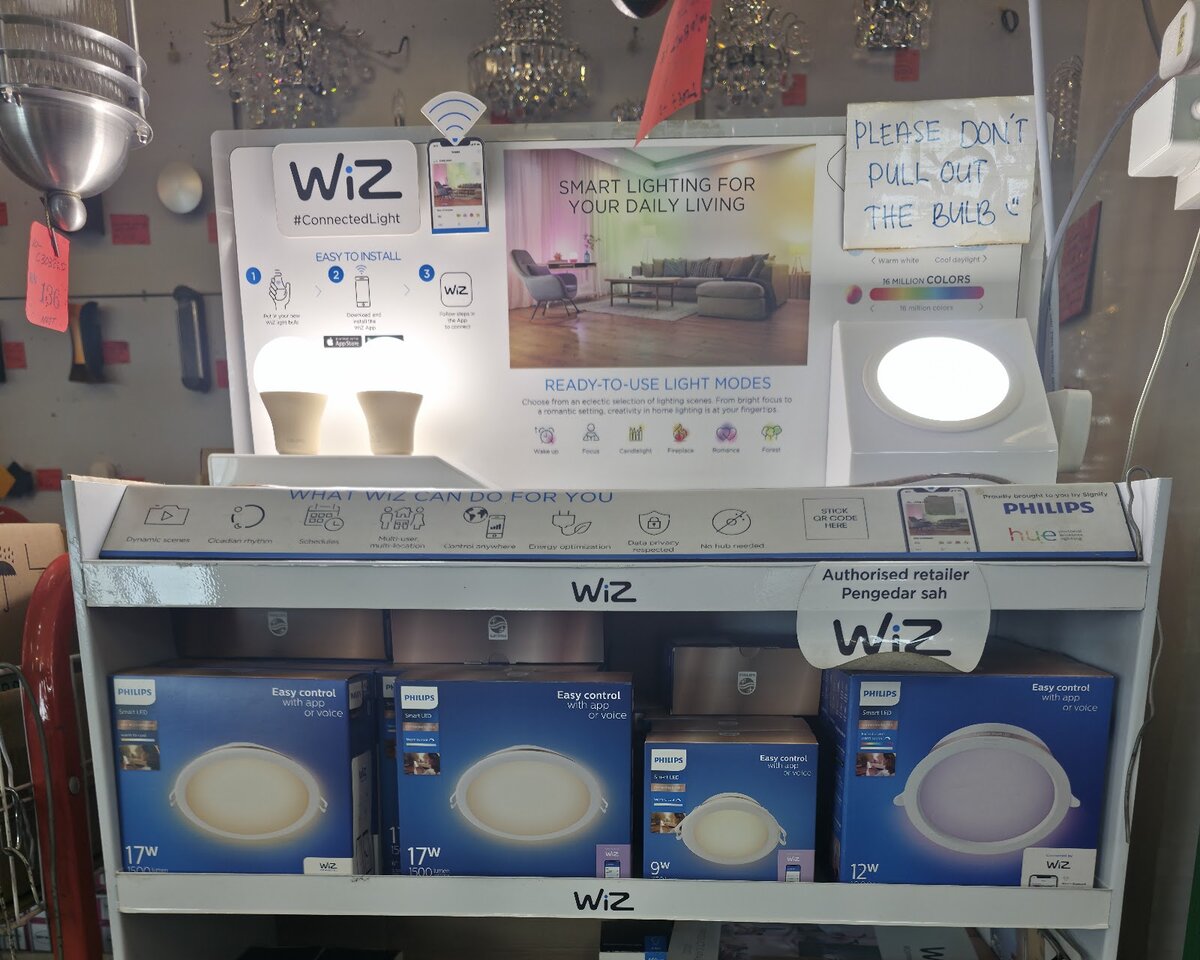 White WiZ display stand with lit sample bulbs, a Philips Hue and WiZ banner and shelves of blue Philips smart downlight boxes