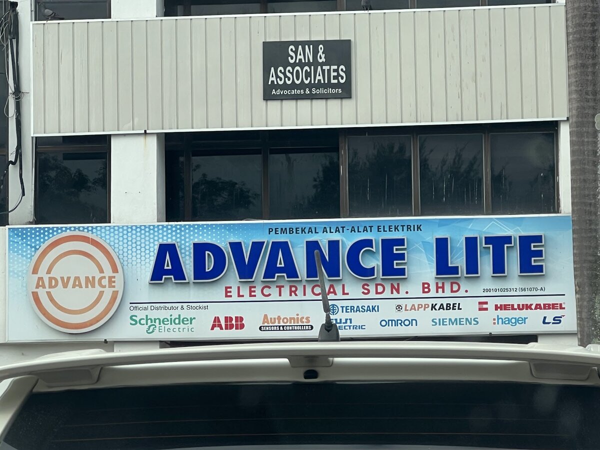 Blue and white shop signboard reading Advance Lite Electrical Sdn Bhd, Pembekal Alat-Alat Elektrik, with a row of electrical brand logos under the words Official Distributor & Stockist