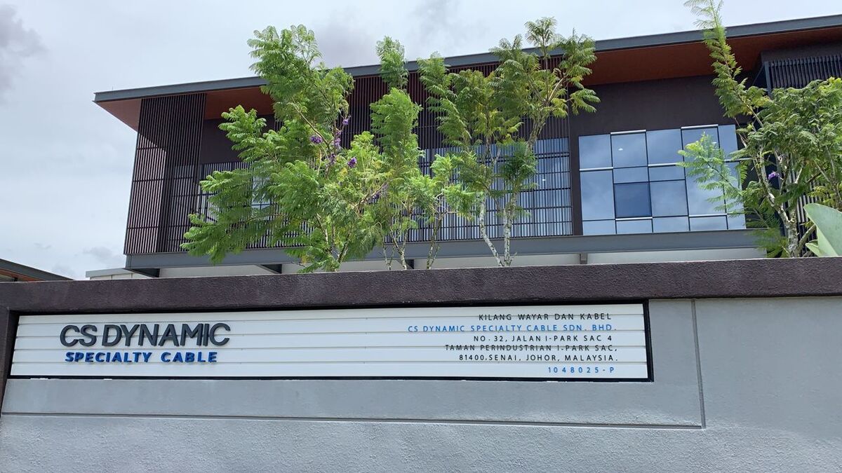 Modern factory building behind a grey boundary wall with a sign reading CS Dynamic Specialty Cable, Kilang Wayar dan Kabel and the Senai address