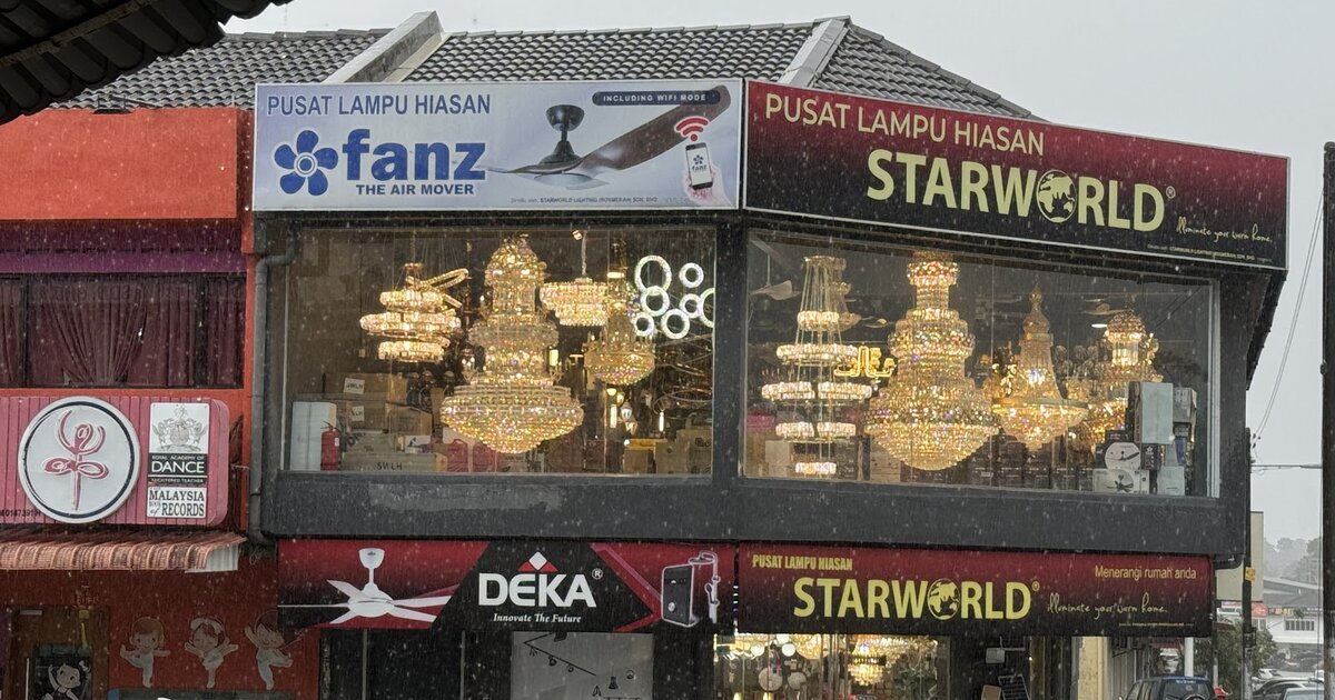 Corner shophouse with red Pusat Lampu Hiasan Starworld signboards, a Fanz fan banner and a Deka banner, and windows full of lit crystal chandeliers