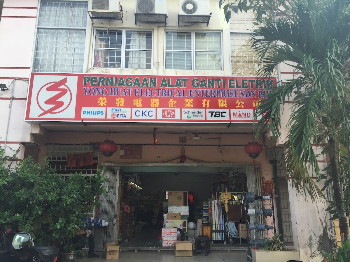 Red signboard reading Perniagaan Alat Ganti Eletrik Yong Huat Electrical Enterprise with brand logos, above an open shop