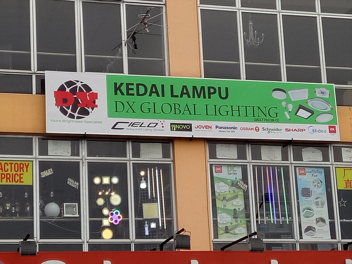 Green and white shop signboard reading Kedai Lampu DX Global Lighting above display windows with lamps and LED tubes