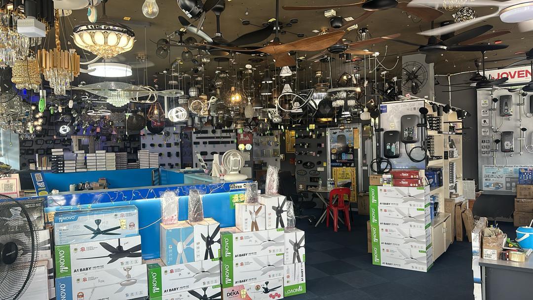 Shop floor crowded with chandeliers and ceiling fans, boxed fans stacked in front of a blue counter and water heaters on a side wall