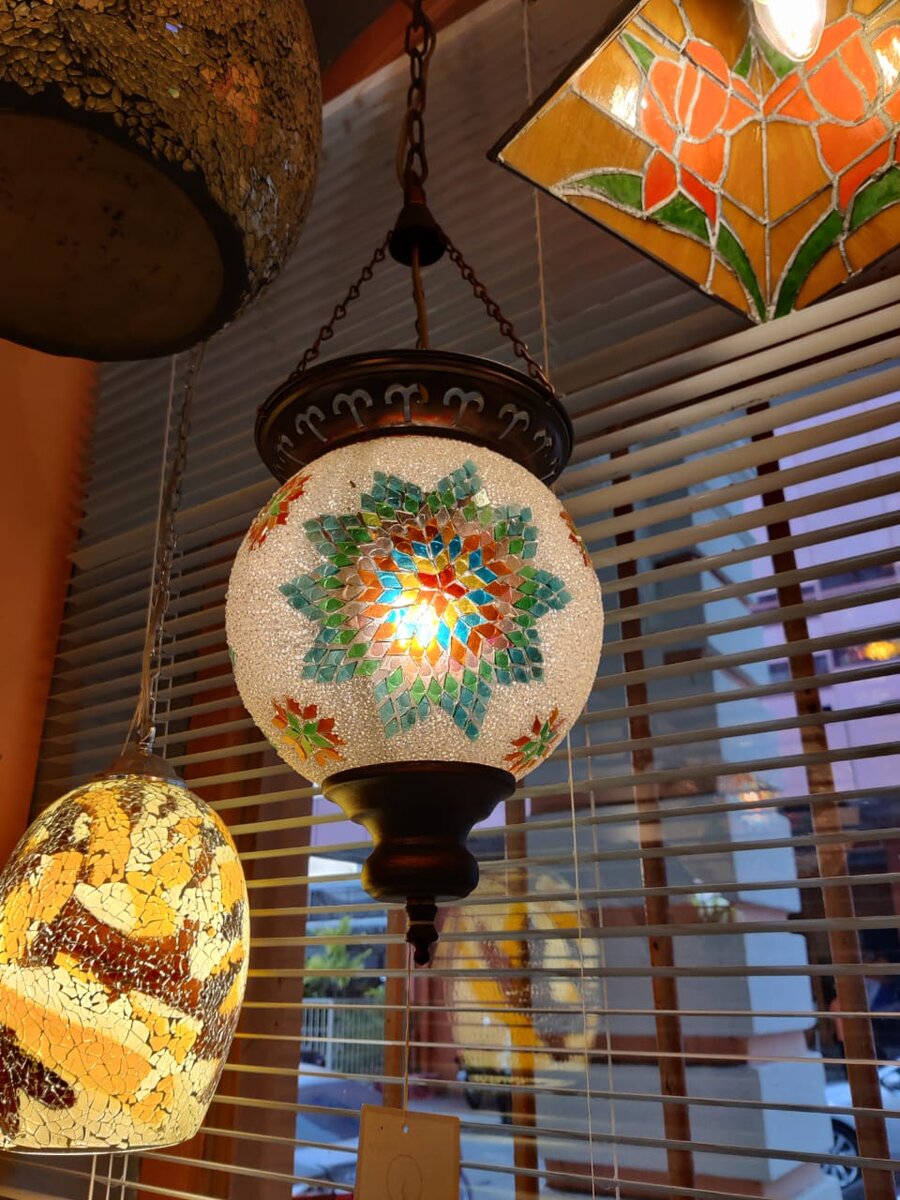 Turkish-style mosaic glass pendant lamps and a stained-glass shade hanging by a window blind