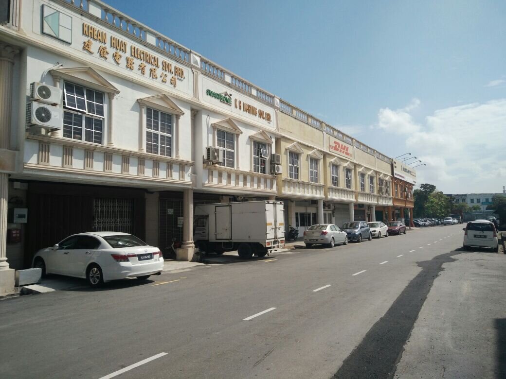 Row of two-storey cream shop offices with gold lettering reading Khean Huat Electrical Sdn. Bhd. and Chinese characters, a green SmartHome logo and K H Lighting Sdn. Bhd. on the neighbouring unit, cars parked along the street