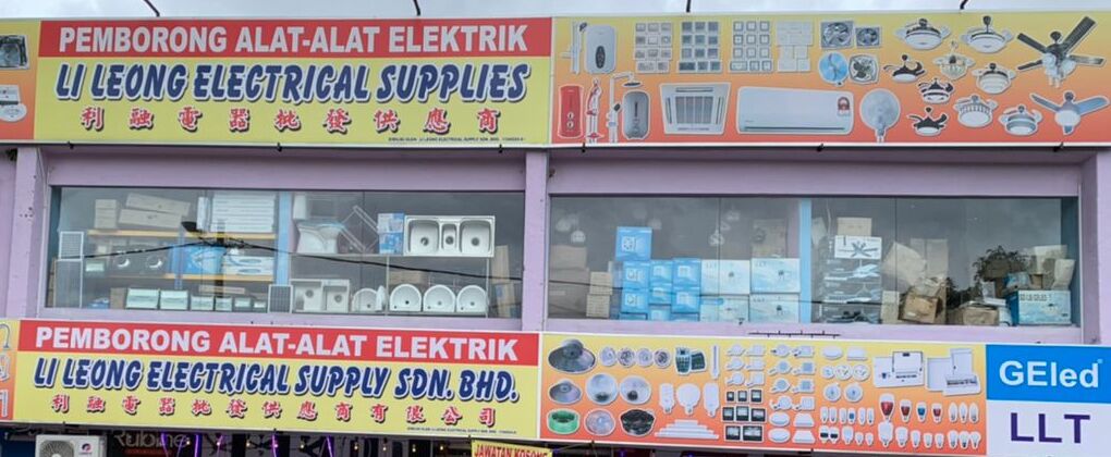 Two rows of yellow Pemborong Alat-Alat Elektrik signboards for Li Leong, with sinks and boxed stock in the upper windows